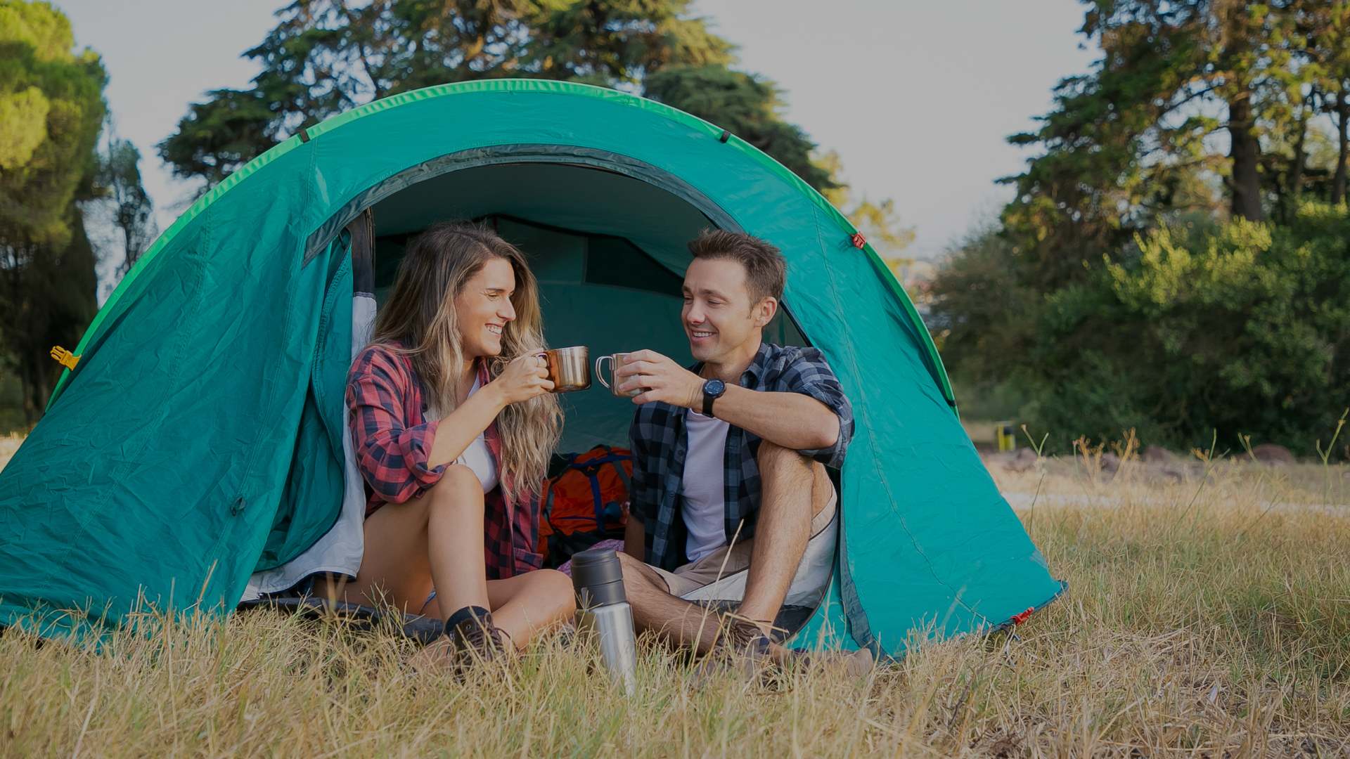 Two people sitting inside a teal camping tent in a natural setting.