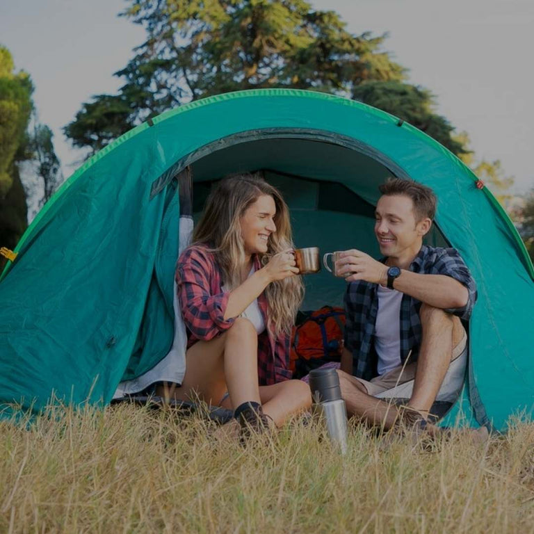 Two people sitting inside a teal camping tent in a natural setting.